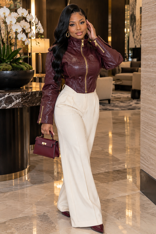 Woman styling burgundy faux leather moto jacket with ivory trousers and burgundy mini handbag